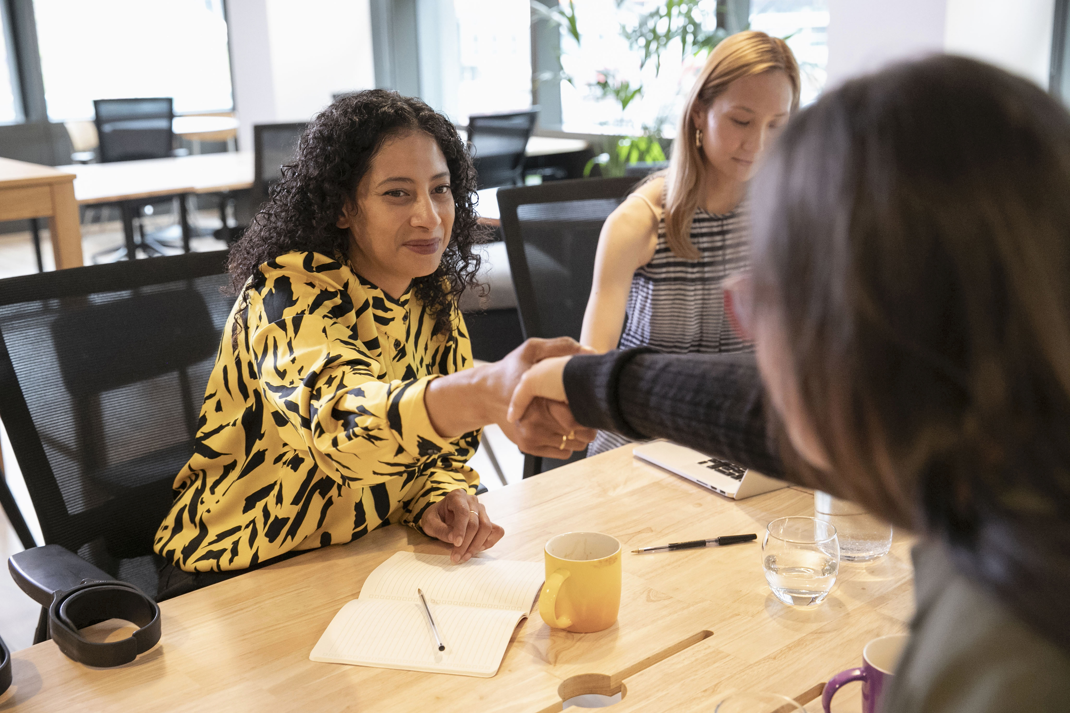 Businesswomen shaking hands over wooden table during team meeting in modern office