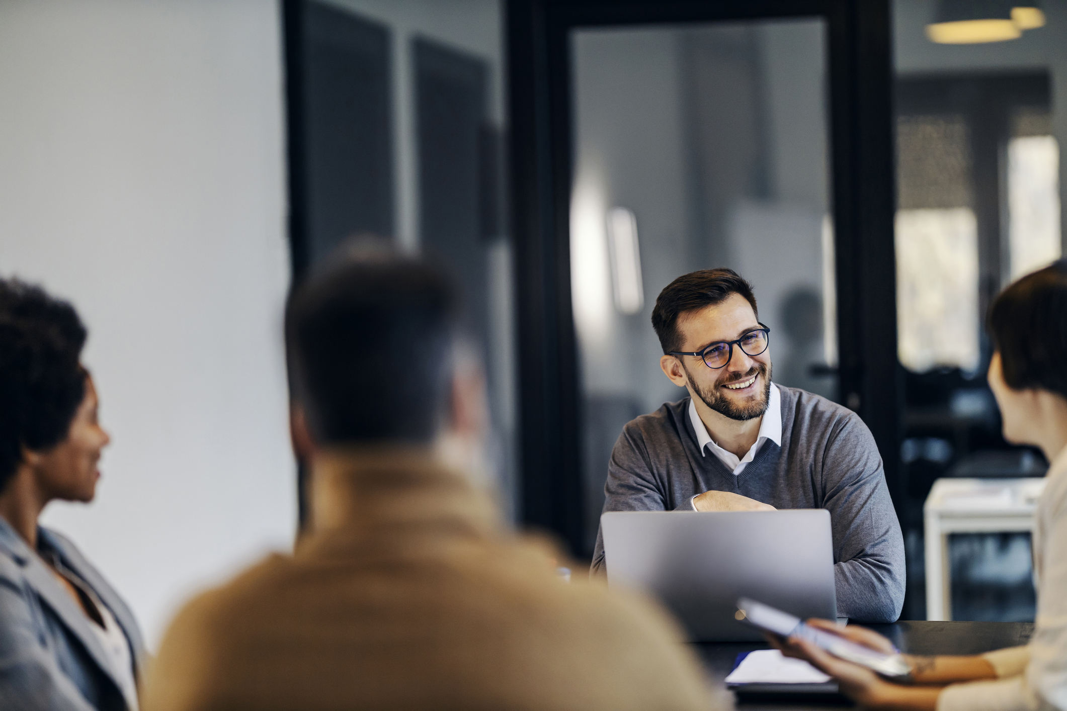A happy manager is sitting in the co working space with colleagues and having business meeting.